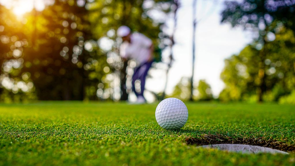 Mastering the Art of Putting [Blog Post] Image shows a golfer in the background, after putting his ball towards the cup on the green.