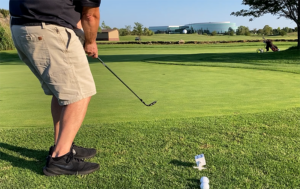 Golfer hitting a pitch shot from behind with the ball in the air on a practice green