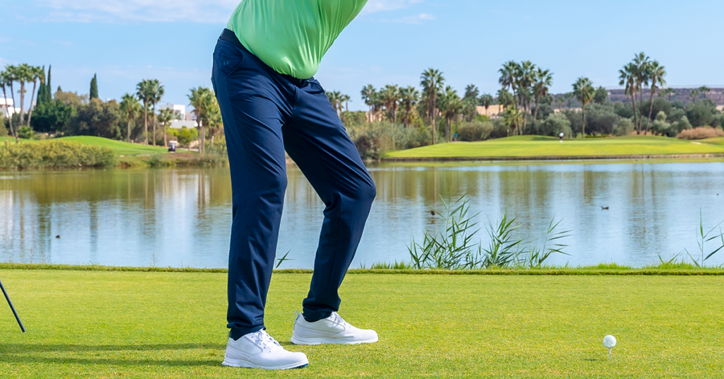 Golfer at the top of the backswing on a tee box over water showing lower body stability and balance